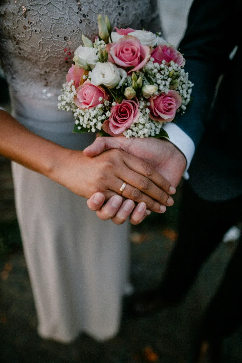 Mariés se tenant la main avec un bouquet de roses roses et blanches